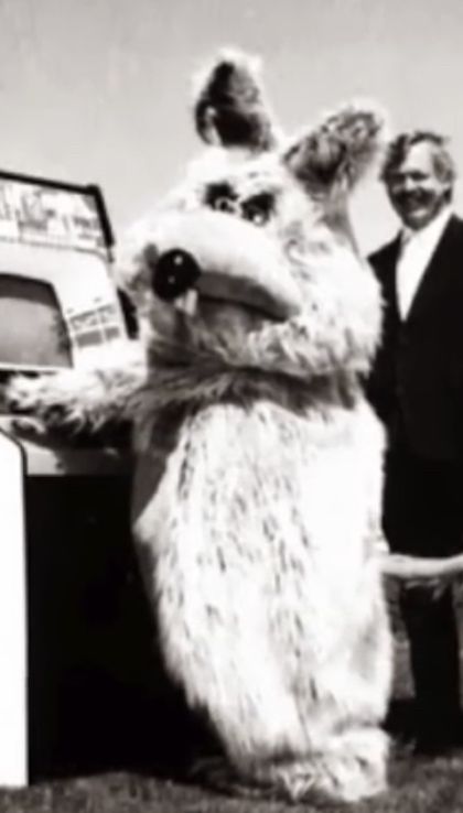 a man standing next to a large stuffed animal in front of a computer monitor and keyboard