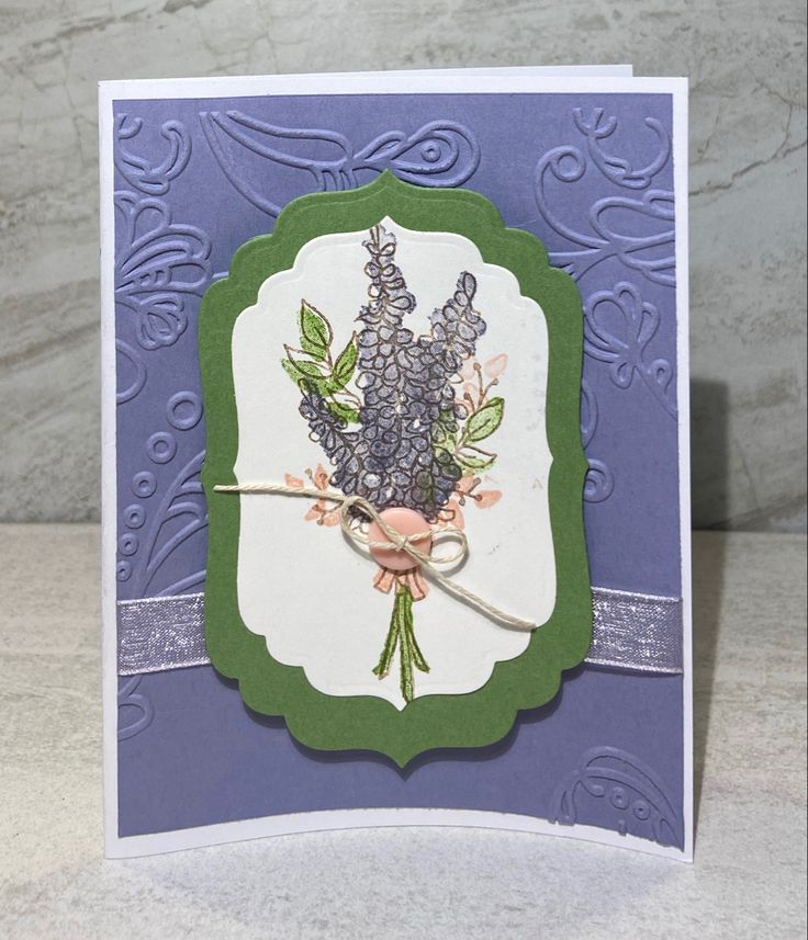 a close up of a card on a table with a white background and purple flowers