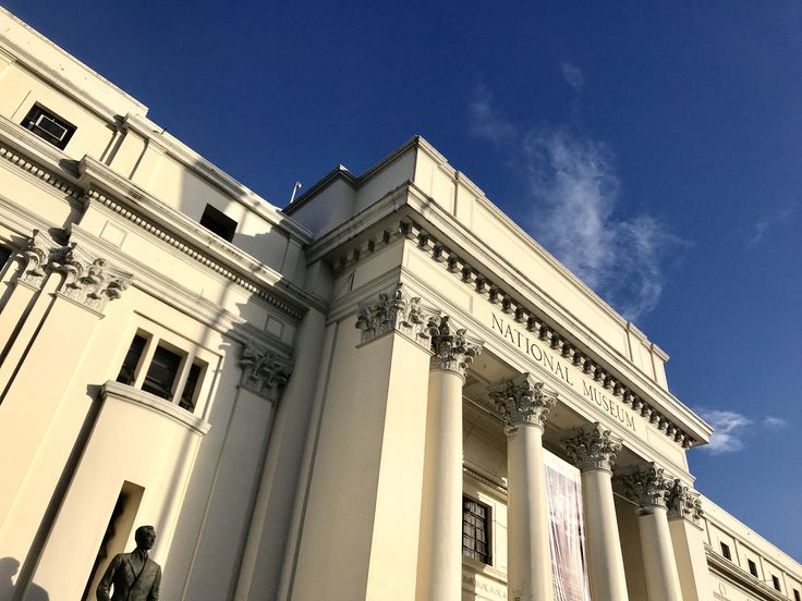 an old building with columns and statues on the front side, against a blue sky