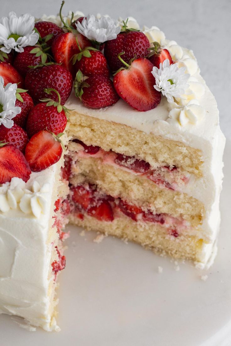 a cake with white frosting and strawberries on top is cut in half to show the layers