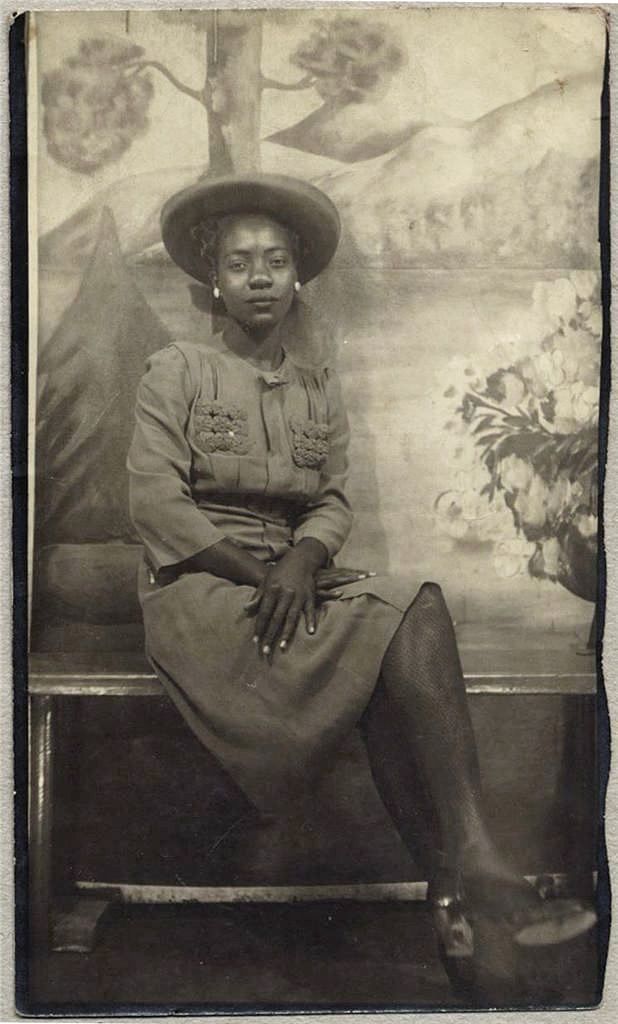 an old black and white photo of a woman wearing a hat sitting on a bench