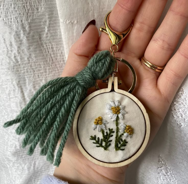 a hand holding a small embroidered keychain with daisies and leaves on it