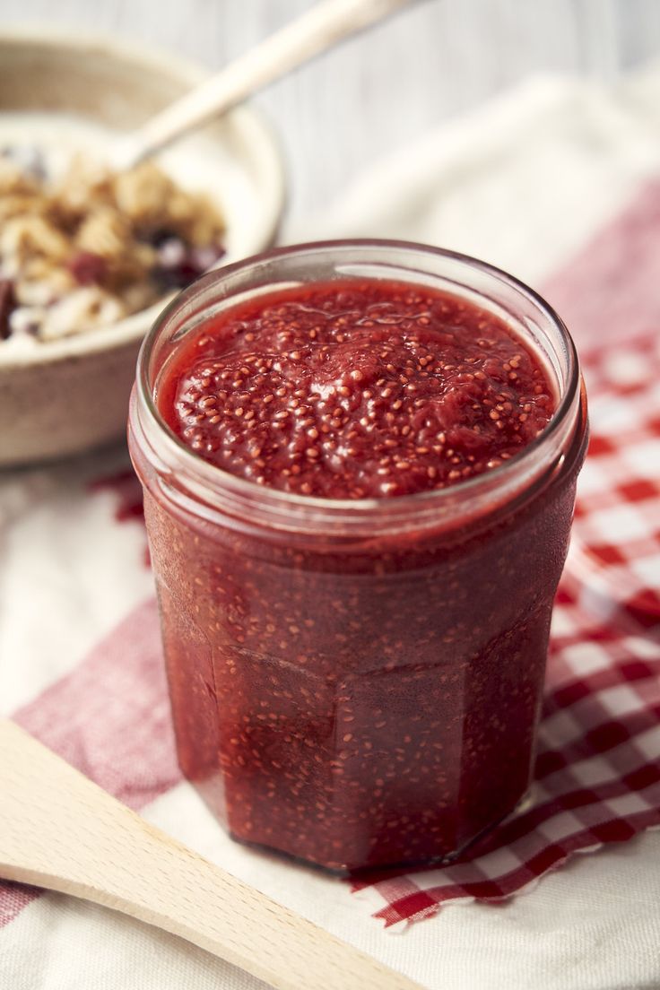 a jar of strawberry jam next to a bowl of oatmeal and spoon