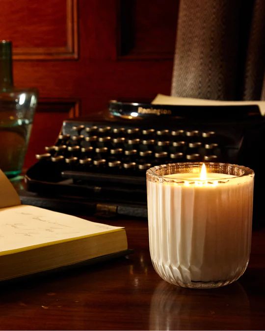 a lit candle sitting on top of a table next to a book and typewriter