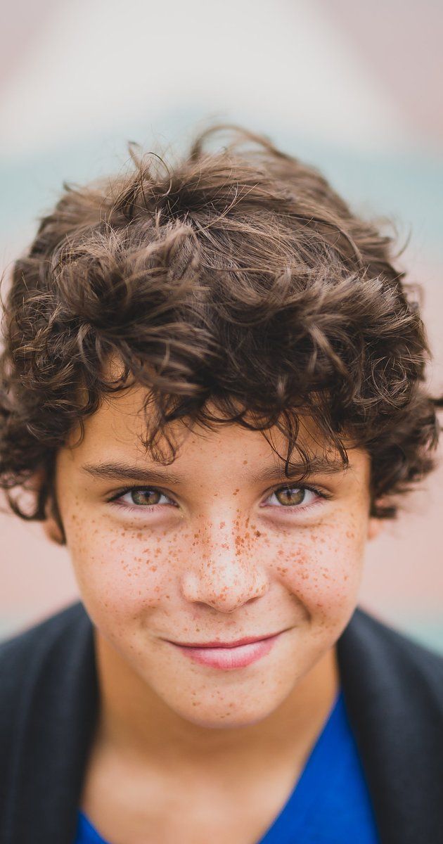 a young boy with freckled hair and blue shirt smiling at the camera while wearing a cardigan