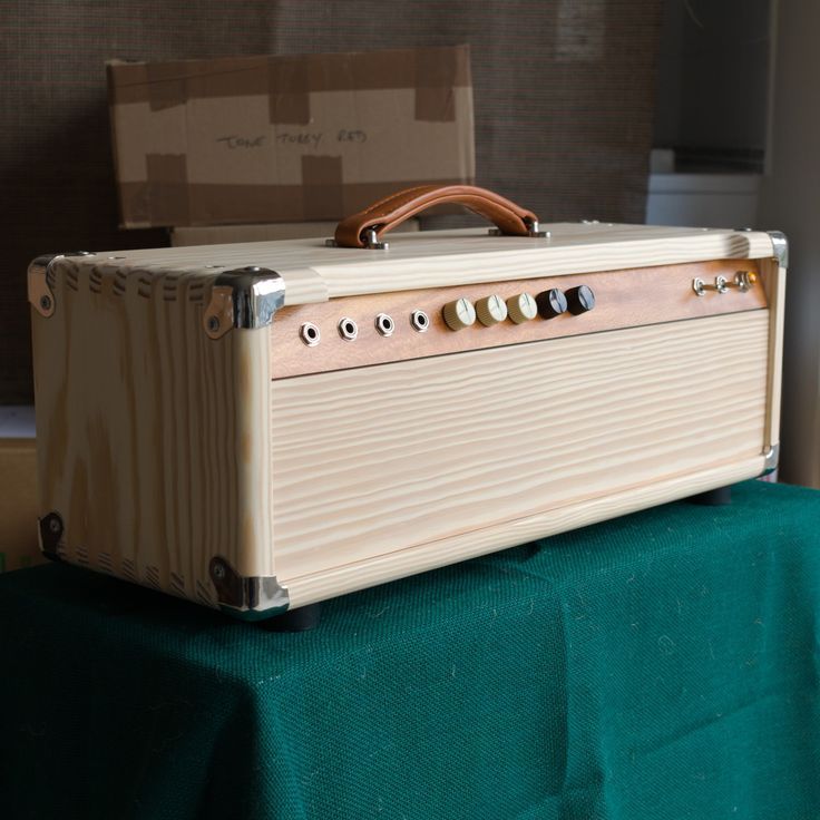 an old style suitcase sitting on top of a green tableclothed cloth with a box in the background