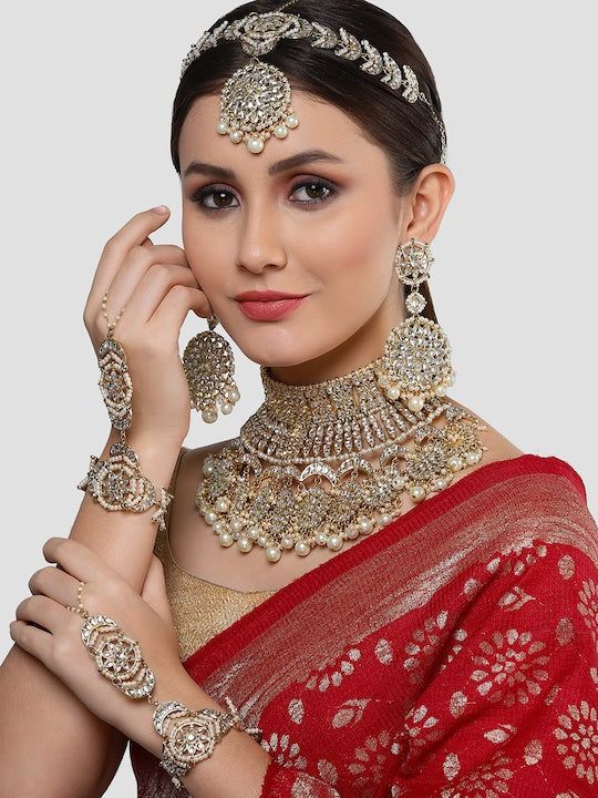 This jewelry set consists of a necklace, a pair of earrings, 2 hathphool bracelets and matha pattiGold-plated necklace has white kundan-studded and white pearls beaded detailsSecured with a drawstring closureA pair of matching drop earrings, each secured with a post-and-back closure2 matching hathphool bracelets, secured with a s-hook closureA matching Matha patti, secured with a hook closure Size & Fit Size of the necklace: 24 cm x 12 cm (Length x Width)Size of the earrings: 11 cm x 5.5 cm(Length x Width)Size of the Mathapatti: 11 cm x 23.5 cm(Length x Width)Size of the Hathphool: 13 cm x 16 cm (Length x Width) Material & Care Material: AlloyPlating: Gold-platedStone Type: Kundan and Beads Care InstructionsWipe your jewellery with a soft cloth after every useAlways store your jewellery in Luxury Festive Jewelry Sets With Latkans, Luxury Cutdana Tikka For Reception, Kundan Bridal Necklace With Latkans, Traditional Kundan Bridal Necklace With Latkans, Heavy Bollywood Jewelry Sets For Puja, Bollywood Heavy Jewelry Sets For Puja, Chandbali Jewelry Sets For Puja, Bollywood Style Jewelry Sets For Puja, Heavy Bridal Sets For Puja And Festive Occasions