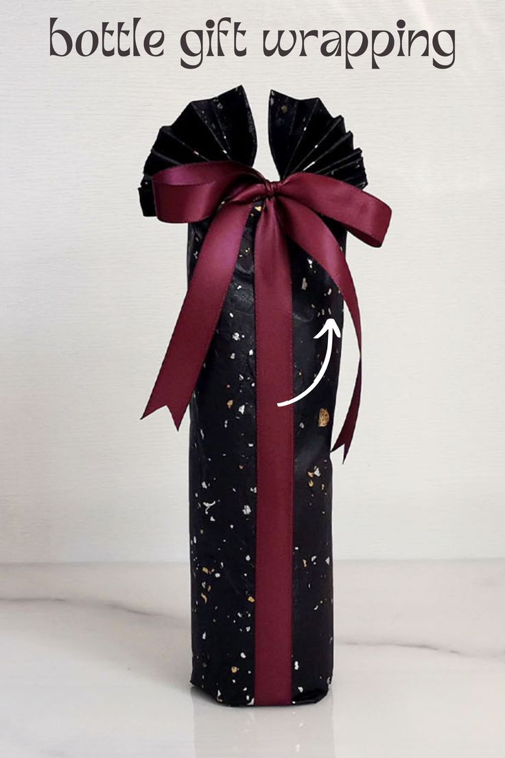 a wine bottle wrapped in black and red paper with a bow on it's side