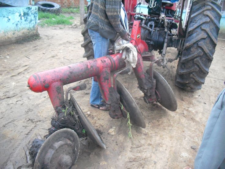 two men standing next to an old red tractor with wheels on the ground near other people