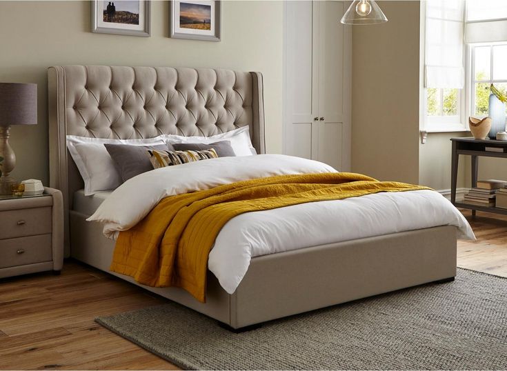 a bedroom with a large bed and yellow blankets on it's headboard, sitting next to a window