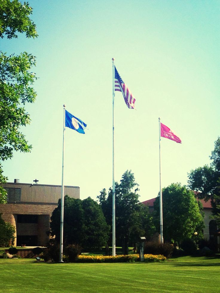 three flags are flying in the wind on a sunny day at an office building with green grass and trees