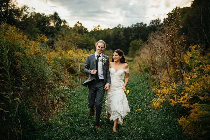 a bride and groom are walking through the grass