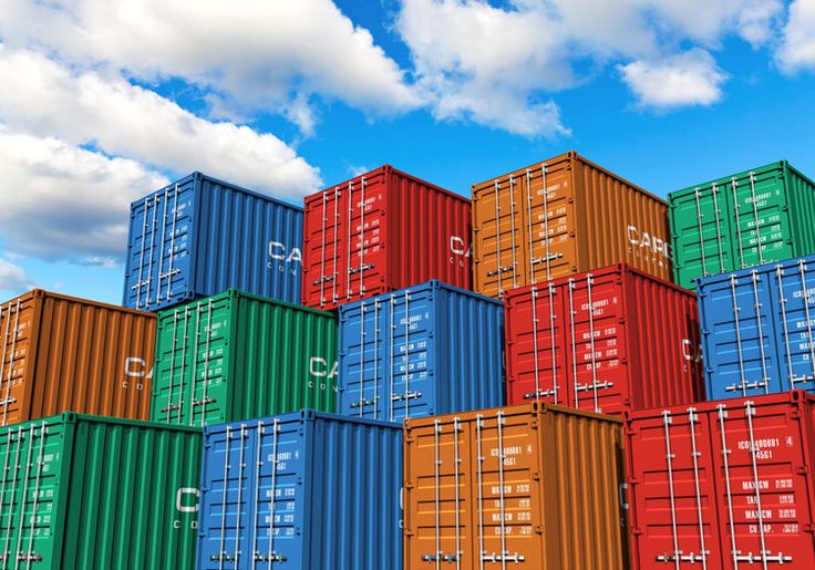 a large stack of multicolored shipping containers against a blue sky with white clouds