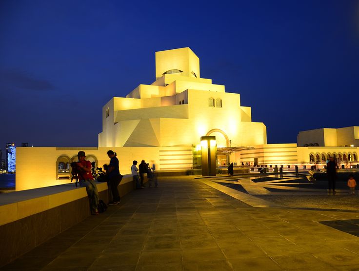 people are standing in front of a white building at night with bright lights on it