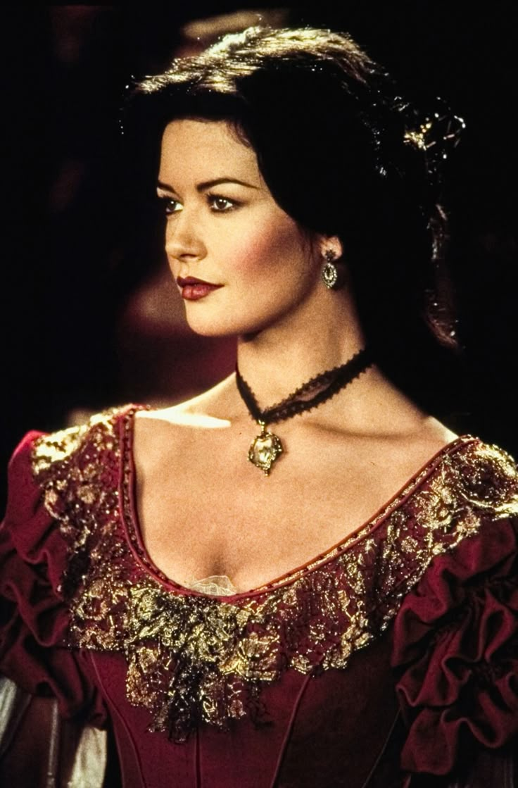 a woman wearing a red dress with gold and black beads on her neck, looking off to the side