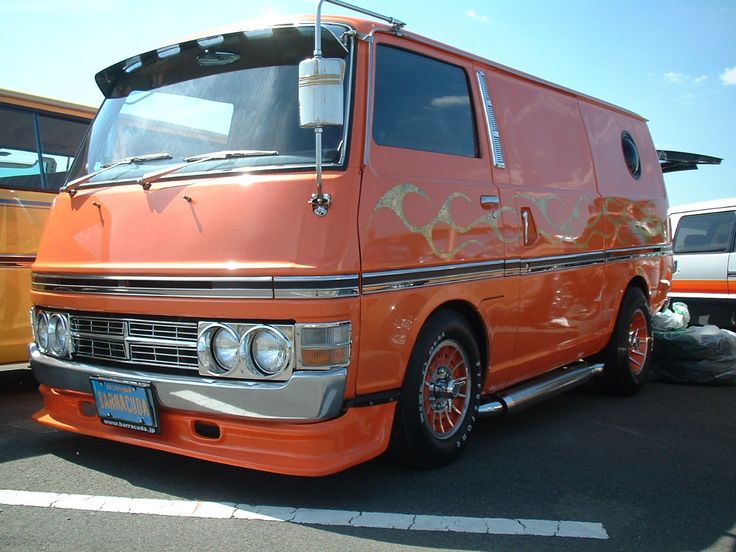 an orange van parked in a parking lot next to other cars and trucks on the street