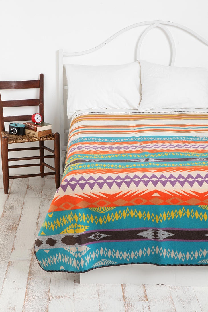 a bed with a colorful blanket on top of it next to a chair and table