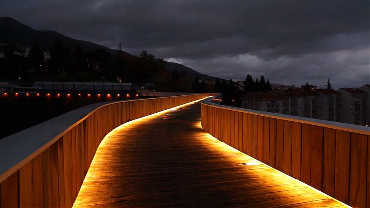 a wooden walkway lit up at night with lights on the sides and dark clouds in the background