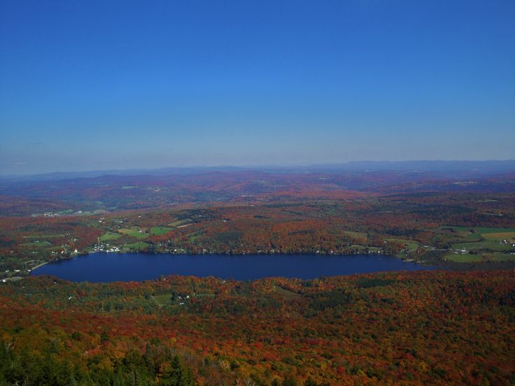 an aerial view of a lake surrounded by trees in the fall with orange and green foliage