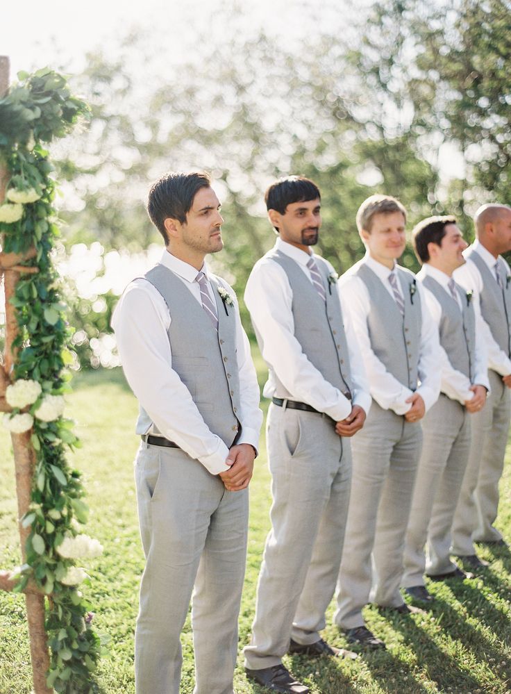 a group of men standing next to each other in front of a wooden arch with flowers on it