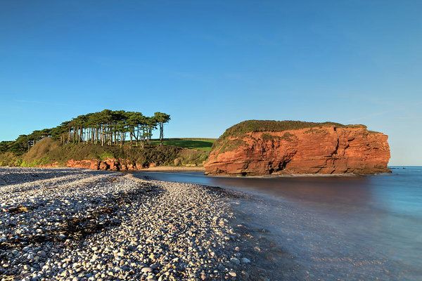 a rocky beach next to the ocean with trees on top of it and an island in the distance