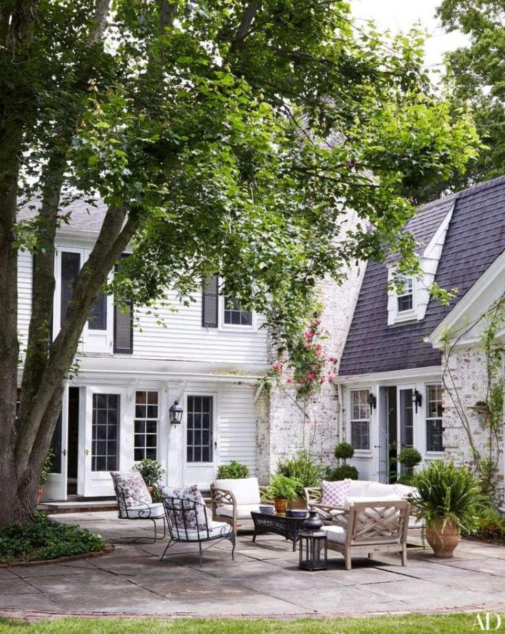 a patio with chairs, tables and potted plants in front of a white house