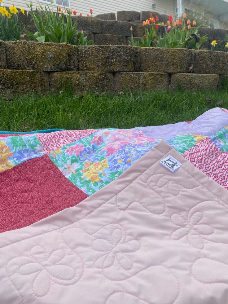 a patchwork quilt is laying on the ground in front of a fence and flowers