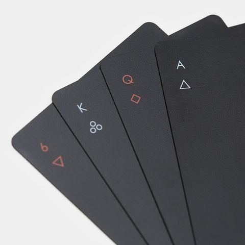 four black playing cards with red numbers and symbols on the front, one in pink