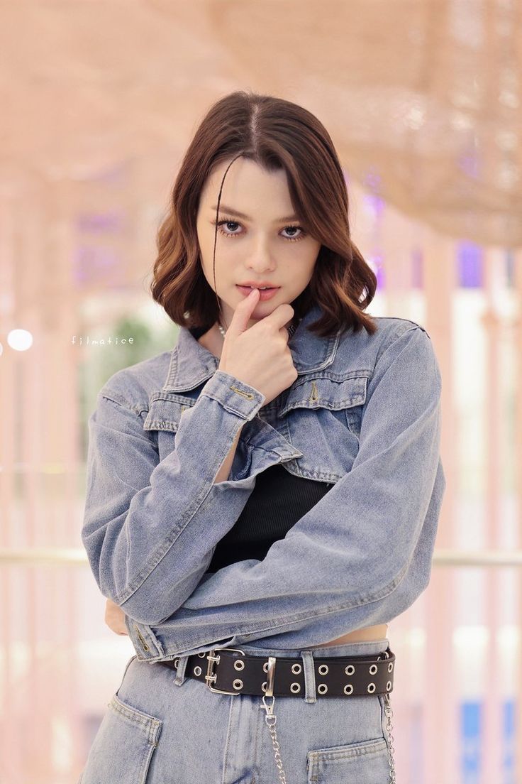 a young woman wearing a jean jacket and jeans posing for a photo with her hand on her chin