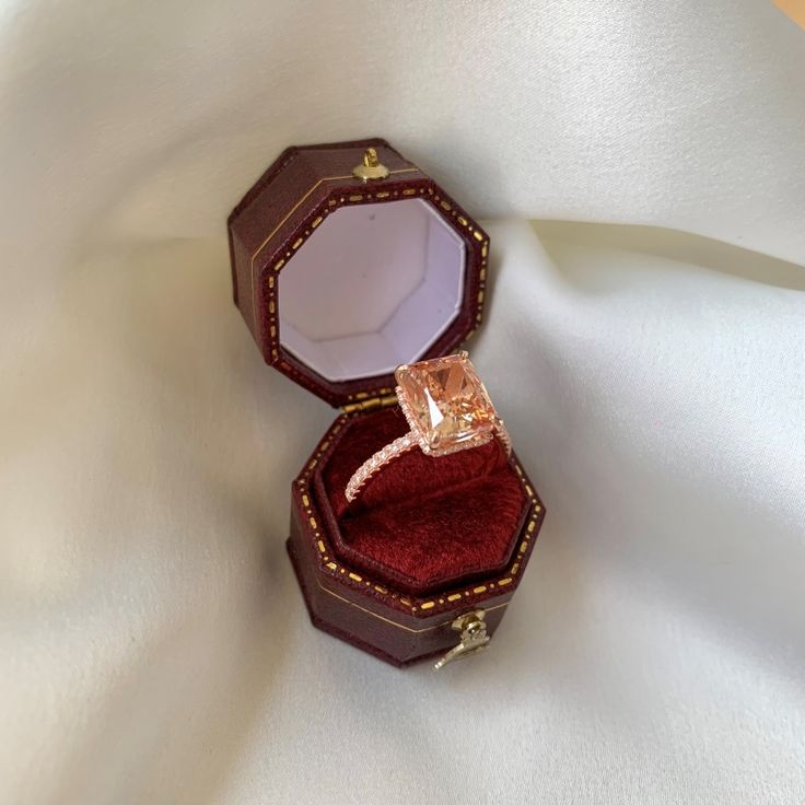 an open ring box sitting on top of a white cloth covered tablecloth with a diamond in it