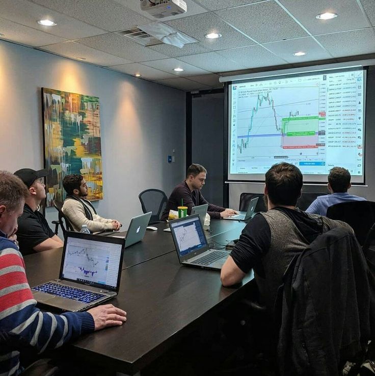 several people sitting at a table with laptops in front of a large projection screen