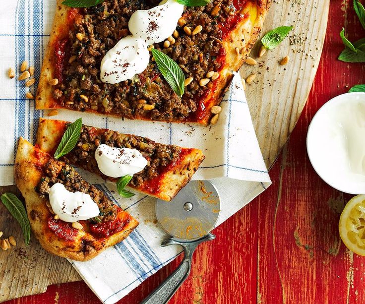 three slices of pizza sitting on top of a wooden cutting board next to a bowl of yogurt