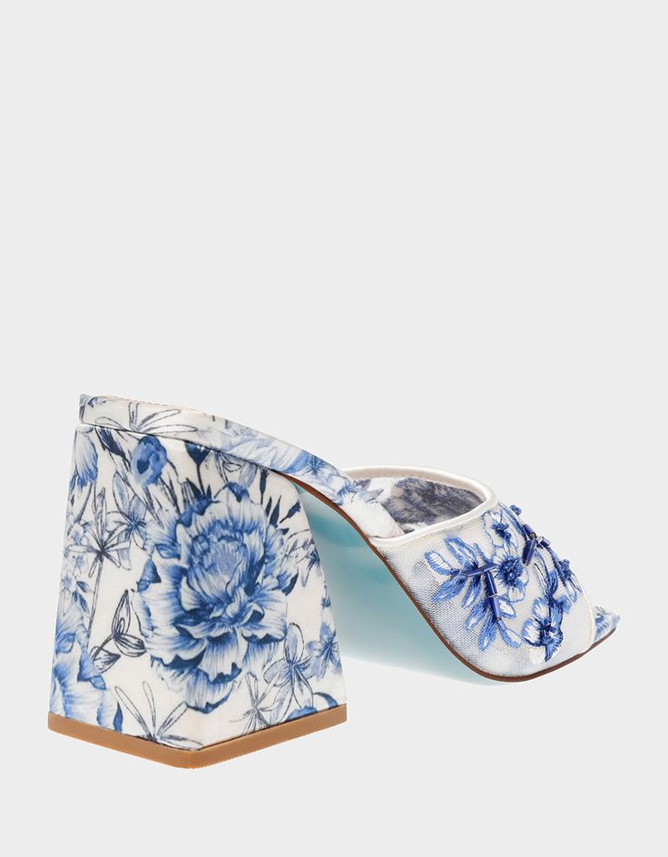 Transform from day to night with the ROO Blue Floral slip-on heel! This stunning sandal features a sturdy block heel and a breezy slip-on toe strap embellished with vibrant blue floral patterns, making it the perfect match for dresses or denim. Mesh textile upper material with beaded embellishments Synthetic lining/sock Synthetic Betsey Blue sole 3.75 inch heel height Imported Spring Slip-on Heels With Heel Strap, Blue Mules With Sculpted Heel For Spring, Blue Spring Mules With Wooden Heel, Blue Mules With Wooden Heel For Spring, Blue Sandals With Stacked Heel For Spring, Spring Slip-on Block Heels With Stacked Heel, Blue Slip-on Heels For Summer, Blue Mules With Stacked Block Heel, Spring Block Heels With Stacked Heel And Slip-on Shape