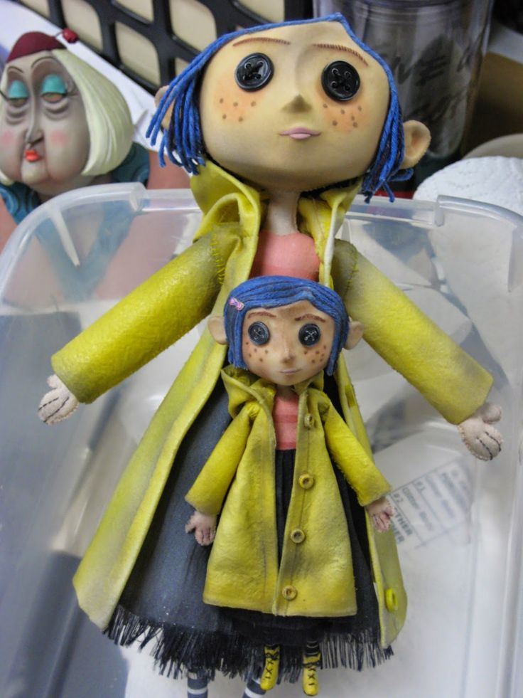 a doll with blue hair is standing next to another doll wearing a yellow coat and black skirt