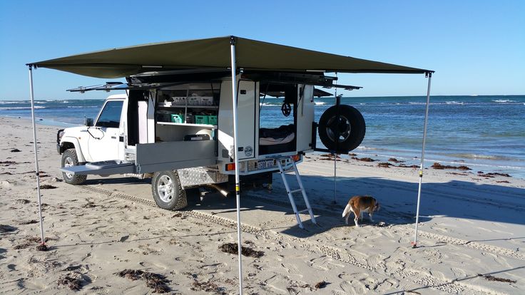 a white truck parked on top of a sandy beach next to the ocean with a dog