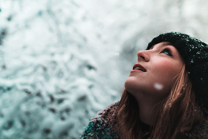 a woman looking up into the sky with snow falling on her head and hair blowing in the wind