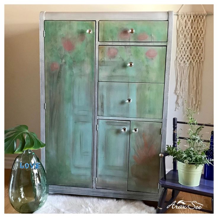 a green cabinet sitting on top of a wooden floor next to a vase with flowers