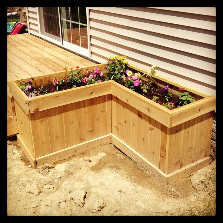 a wooden planter box sitting on top of a dirt ground next to a house