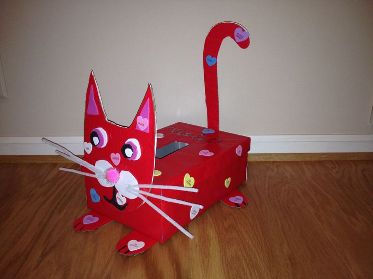 a cat made out of cardboard sitting on top of a wooden floor next to a box