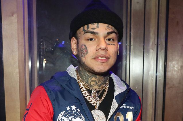 a young man with tattoos and piercings standing in front of a door wearing a jacket