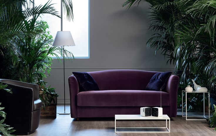 a living room with purple couches and potted plants on the side table in front of it