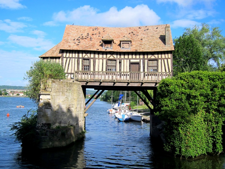 an old house sitting on top of a bridge over a body of water with boats floating underneath it