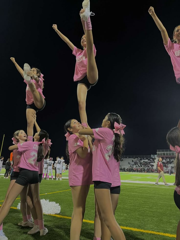 a group of cheerleaders in pink shirts doing tricks on the field at night