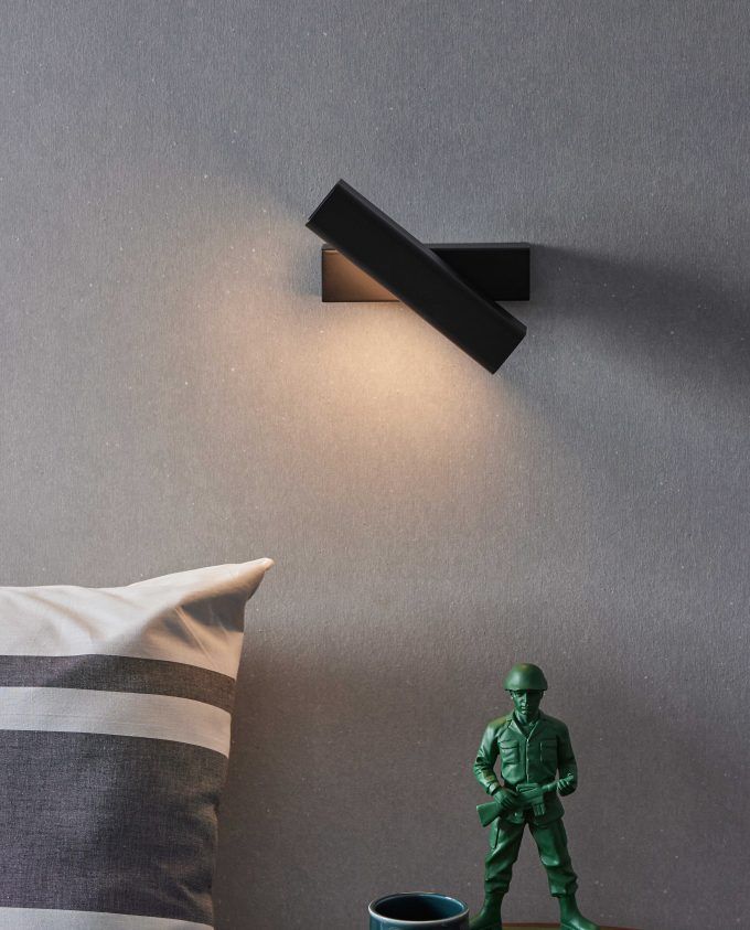 a green toy soldier standing next to a pillow and lamp on the wall in a bedroom