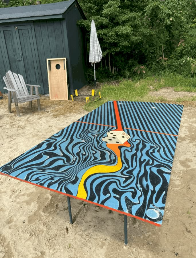 a table that has been painted to look like a painting on the ground with an umbrella and chair in the background