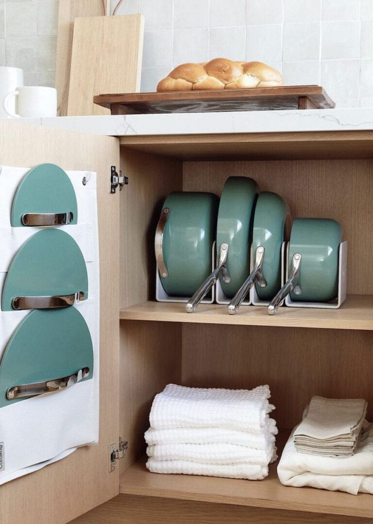 an open cabinet with dishes and pans on the bottom shelf, next to some bread rolls