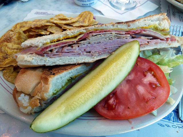 a sandwich and chips on a plate with a pickle, tomato and lettuce