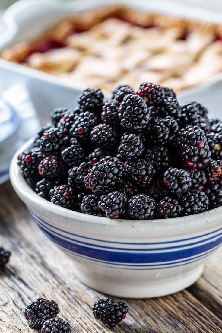 a bowl filled with blackberries sitting on top of a wooden table