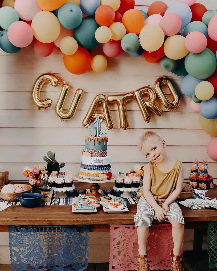 a young boy sitting at a table in front of a birthday cake and balloon garland