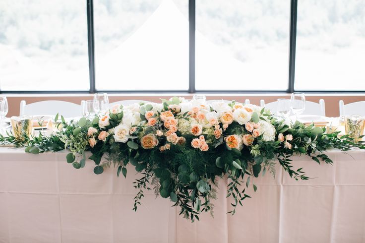 an arrangement of flowers and greenery is arranged on a table with white linens